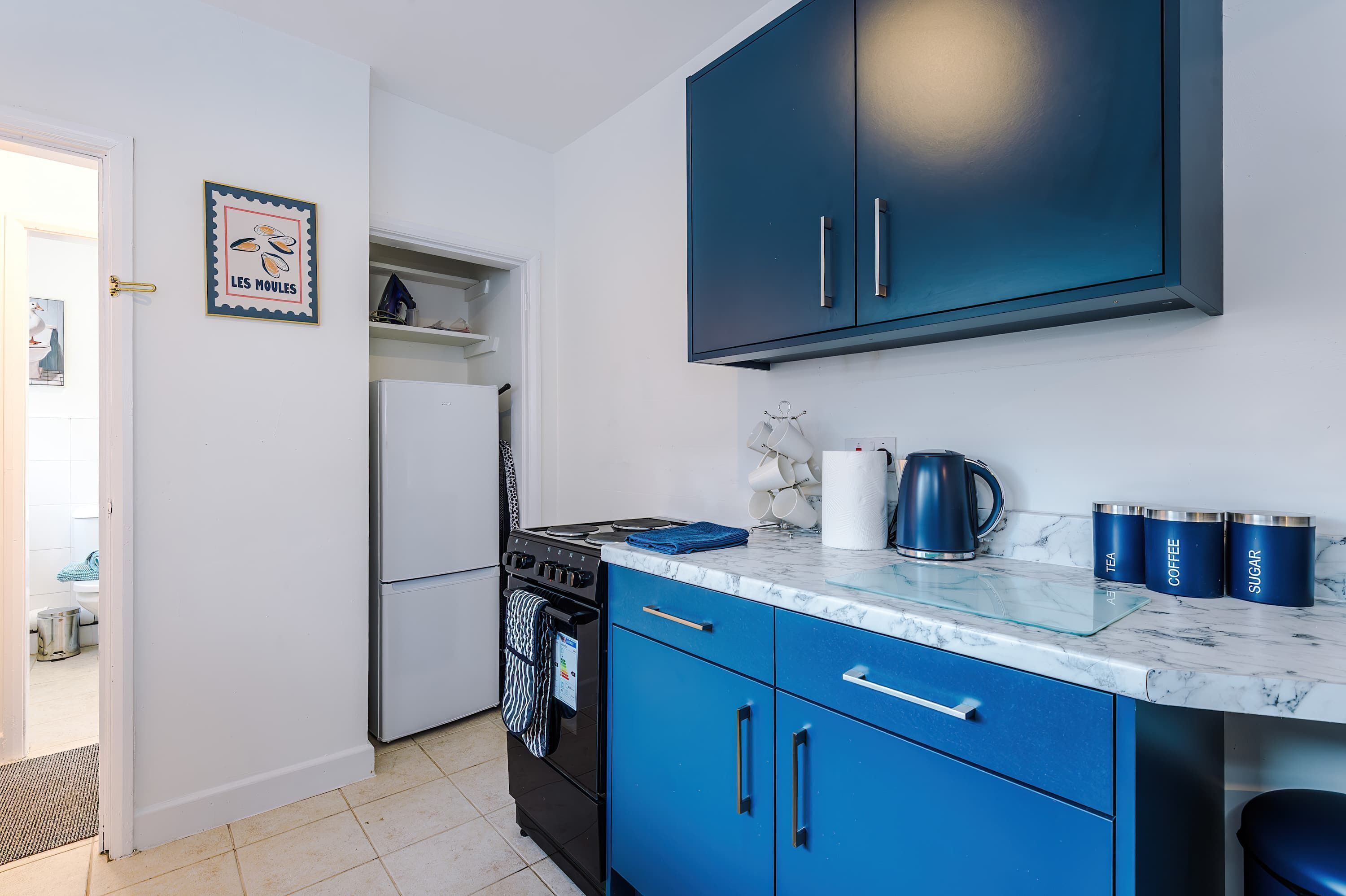 A kitchen with blue cabinets, a white refrigerator, a stove, and a marble countertop.
