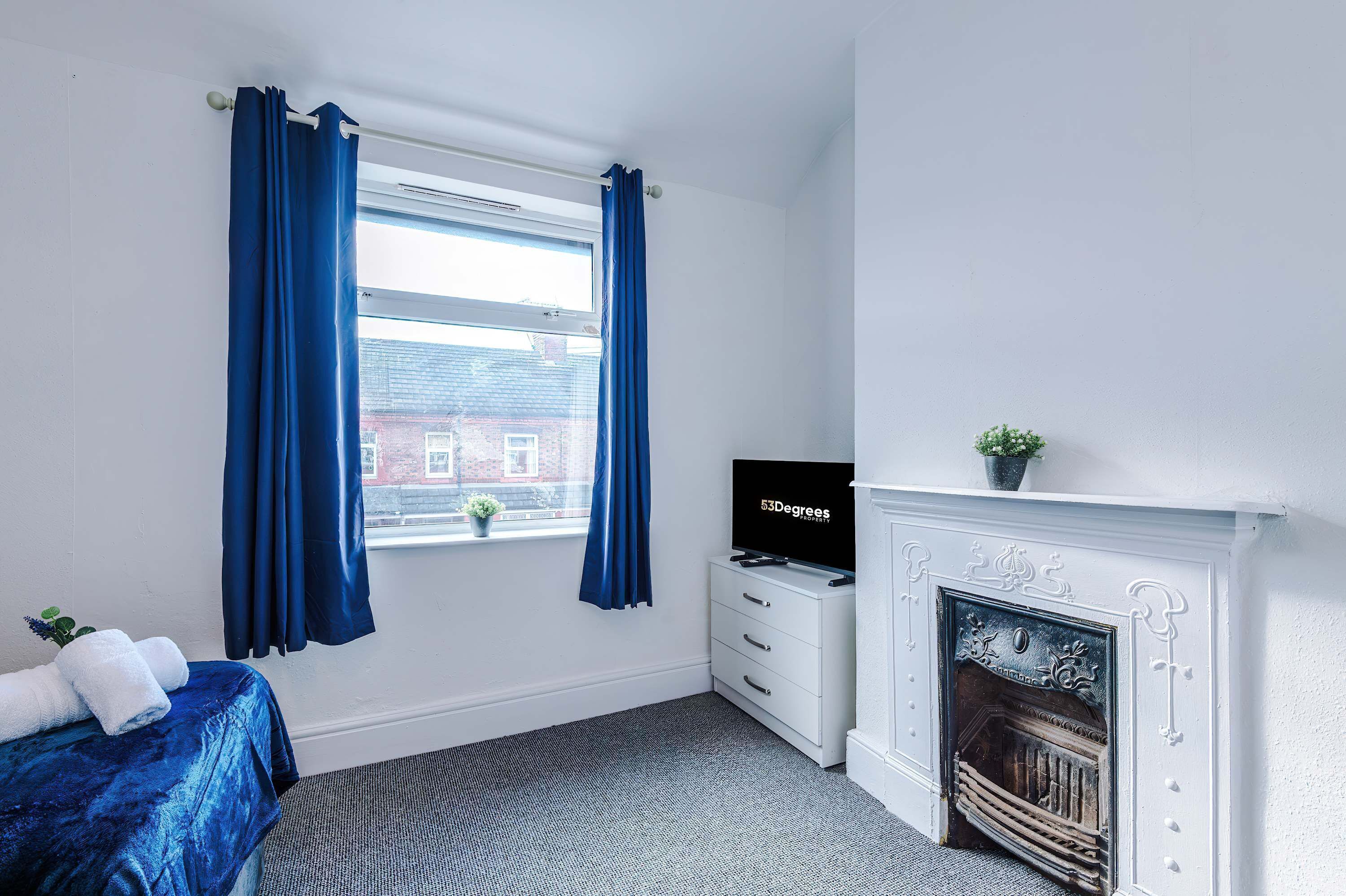 A room with a bed, a television, a fireplace, and a window with curtains.
