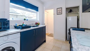 A kitchen with a washing machine, a microwave, and a window with a blue blind. - Great 3-bed Home Perfect for Work Contractors (Ellesmere Port)