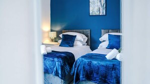 A hotel room with two beds, a nightstand with a lamp, and a painting on the wall. - Great 3-bed Home Perfect for Work Contractors (Ellesmere Port)