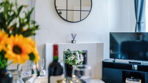 A modern living room with a fireplace, a round mirror, a television, and a dining area with a vase of flowers. - Great 3-bed Home Perfect for Work Contractors (Ellesmere Port)