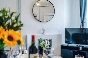 A modern living room with a fireplace, a round mirror, a television, and a dining area with a vase of flowers. - Great 3-bed Home Perfect for Work Contractors (Ellesmere Port)