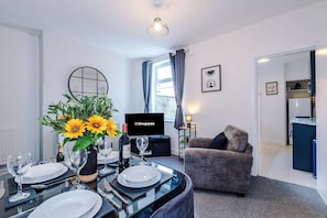 A modern hotel room with a dining area, a sofa, a TV, and a kitchen area. - Great 3-bed Home Perfect for Work Contractors (Ellesmere Port)