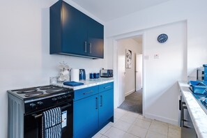 A modern kitchen with blue cabinets, a stove, and a microwave. - Great 3-bed Home Perfect for Work Contractors (Ellesmere Port)