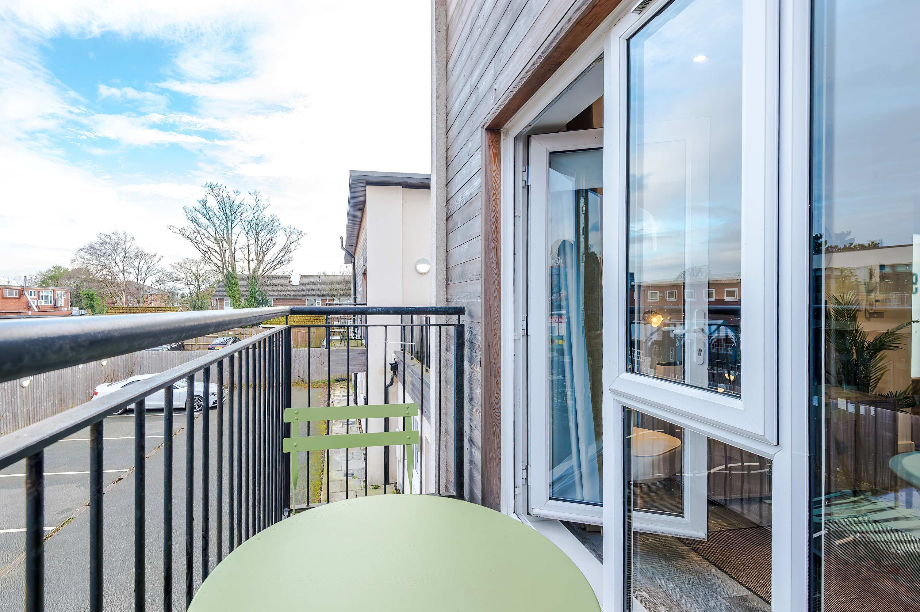 A balcony with a view of the street, a glass door, and a small outdoor seating area.