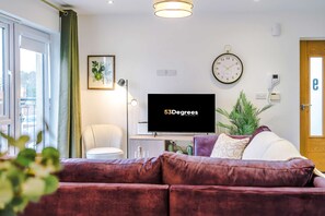A living room with a television, a clock, a plant, and a door. - Centrally Located Flat off Formby High Street (Liverpool)