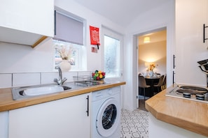 A compact kitchen with a washing machine, a sink, and a window with a view. - Central 2 Bed in Wrexham Sleeps 6 With Parking (Wrexham)