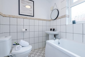 A bathroom with a toilet, sink, and bathtub, tiled walls, and a framed picture on the wall. - Central 2 Bed in Wrexham Sleeps 6 With Parking (Wrexham)