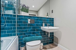 Ein Badezimmer mit Dusche, Toilette und Waschbecken, mit blauen Fliesen und einer weißen Arbeitsplatte.
