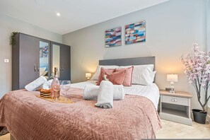 Ein ordentlich gemachtes Bett mit einer rosa Decke, ein Nachttisch mit einer Lampe, ein Beistelltisch mit einer Pflanze und ein Kleiderschrank.