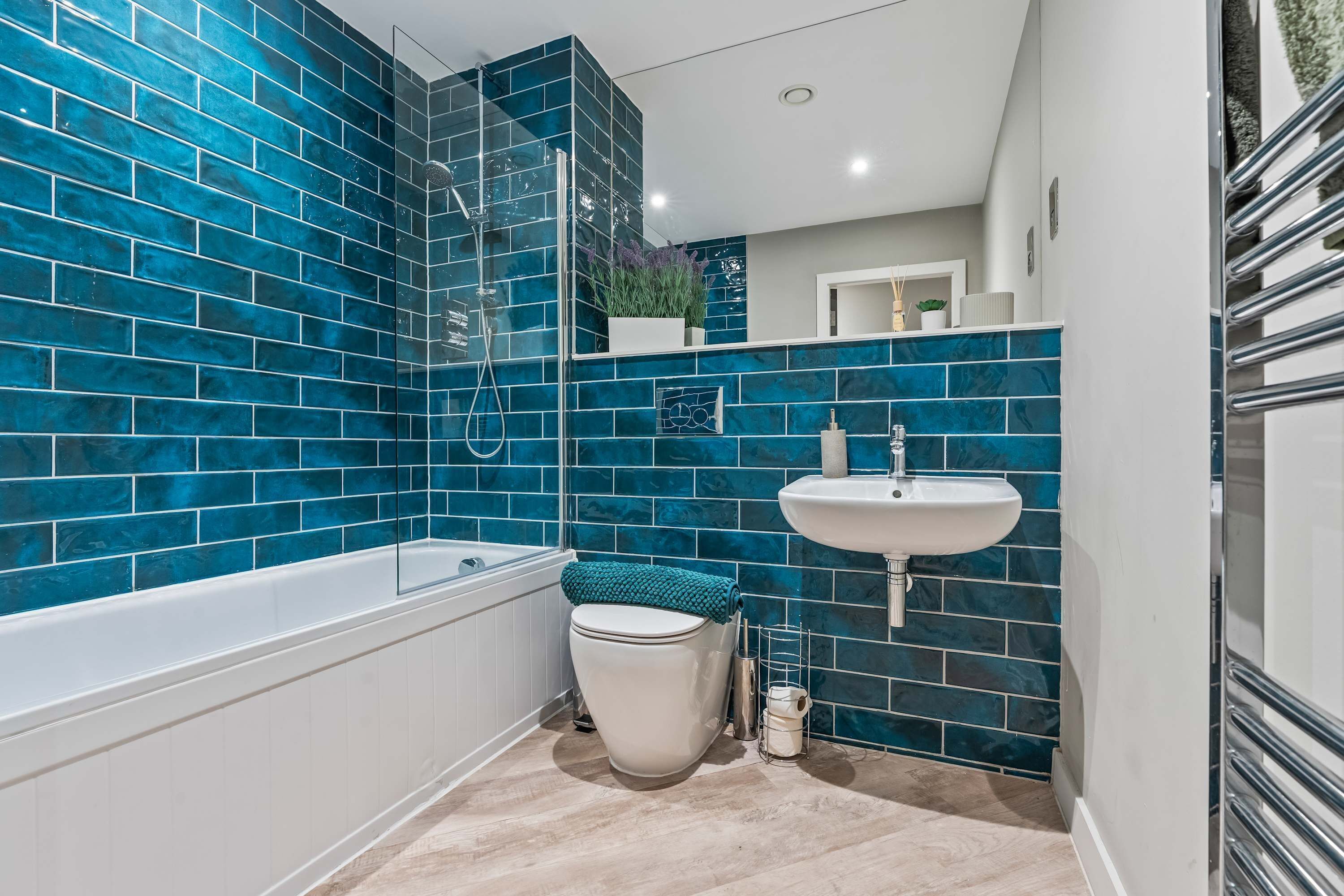 A bathroom with blue-tiled walls, a white bathtub, a white toilet, and a white sink.