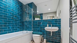 A bathroom with blue-tiled walls, a white bathtub, a white toilet, and a white sink. - Stylish 1 Bed Flat in Birmingham City Centre (Birmingham)