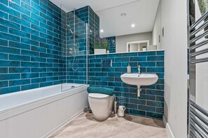 Ein Badezimmer mit blauen Fliesen, einer weißen Badewanne, einer weißen Toilette und einem weißen Waschbecken.