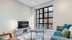 A modern living room with a TV, a small round table, a sofa, and a large window. - Stylish 1 Bed Flat in Birmingham City Centre (Birmingham)