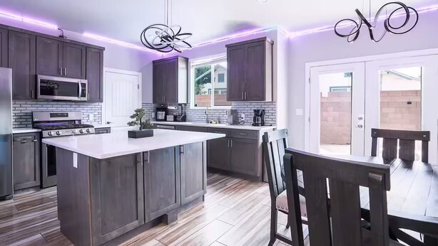 Una cucina moderna con mobili scuri, un'isola centrale, elettrodomestici in acciaio inossidabile e illuminazione a sospensione.