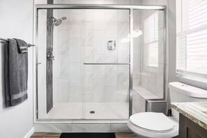 Casa de banho moderna com chuveiro em cabine de vidro, sanita e lavatório com bancada de mármore.