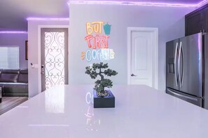 Uma cozinha moderna com um letreiro de neon, uma geladeira e um bonsai na bancada.