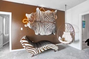 Quarto com arte na parede estampada em zebra, uma cadeira suspensa e um sofá com padrão de zebra.