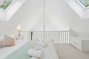Ein Schlafzimmer mit Dachfenster, einem Bett mit Kissen, einem Nachttisch mit Lampe und einer weißen Kommode.