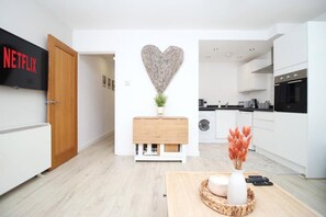 Eine moderne Küche mit weißen Schränken, einer Wanddekoration in Herzform und einem Holzschrank mit einer Pflanze.