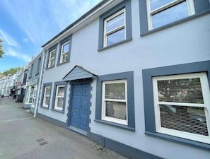 Eine Reihe von Reihenhäusern mit blauer Tür, Fenstern in weißen Rahmen und einer grauen Fassade.