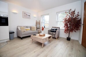 Ein modernes Wohnzimmer mit einer Couch, einem Couchtisch, einem gestreiften Sessel, einer Topfpflanze und einer Küchenzeile mit einem Backofen.