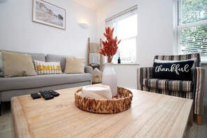 A living room with a sofa, armchair, coffee table, and a vase with dried flowers. - Stylish 1-bed Flat at Irvine Court Sleeps 4 (Swansea)