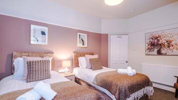Habitación de hotel con dos camas, una puerta blanca y un cuadro grande con motivos florales en la pared.