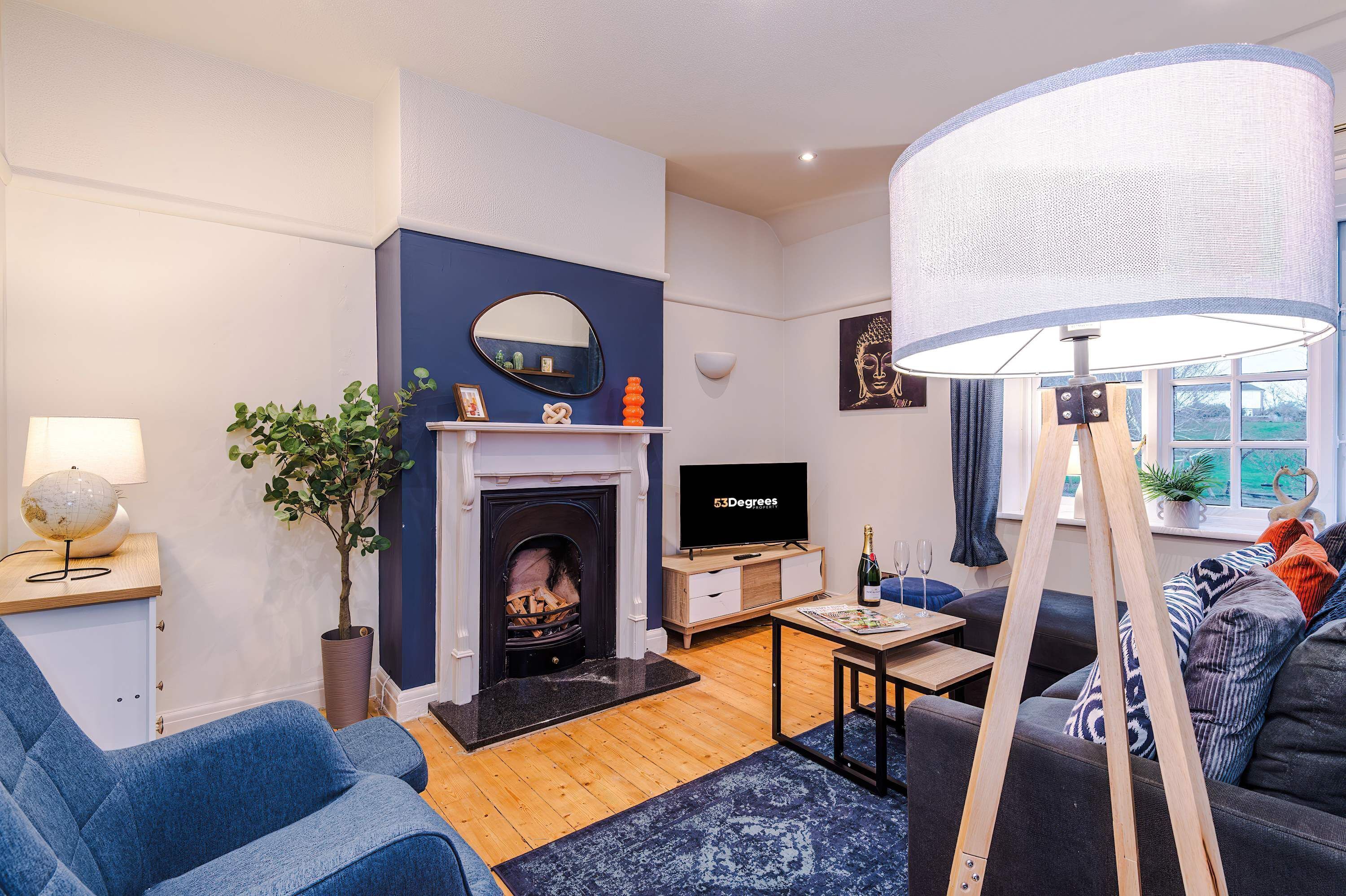 Una sala de estar con chimenea, televisor, sofá, lámpara y ventana con vistas.