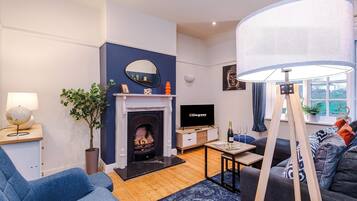 Una sala de estar con chimenea, televisor, sofá, lámpara y ventana con vistas.