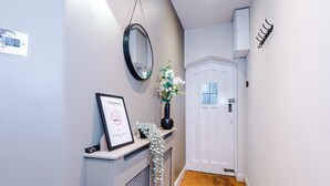 A hallway with a white door, a black-framed mirror, a framed certificate, and a small potted plant. - Charming City Centre 3 Bed Flat High St Location (Chester)