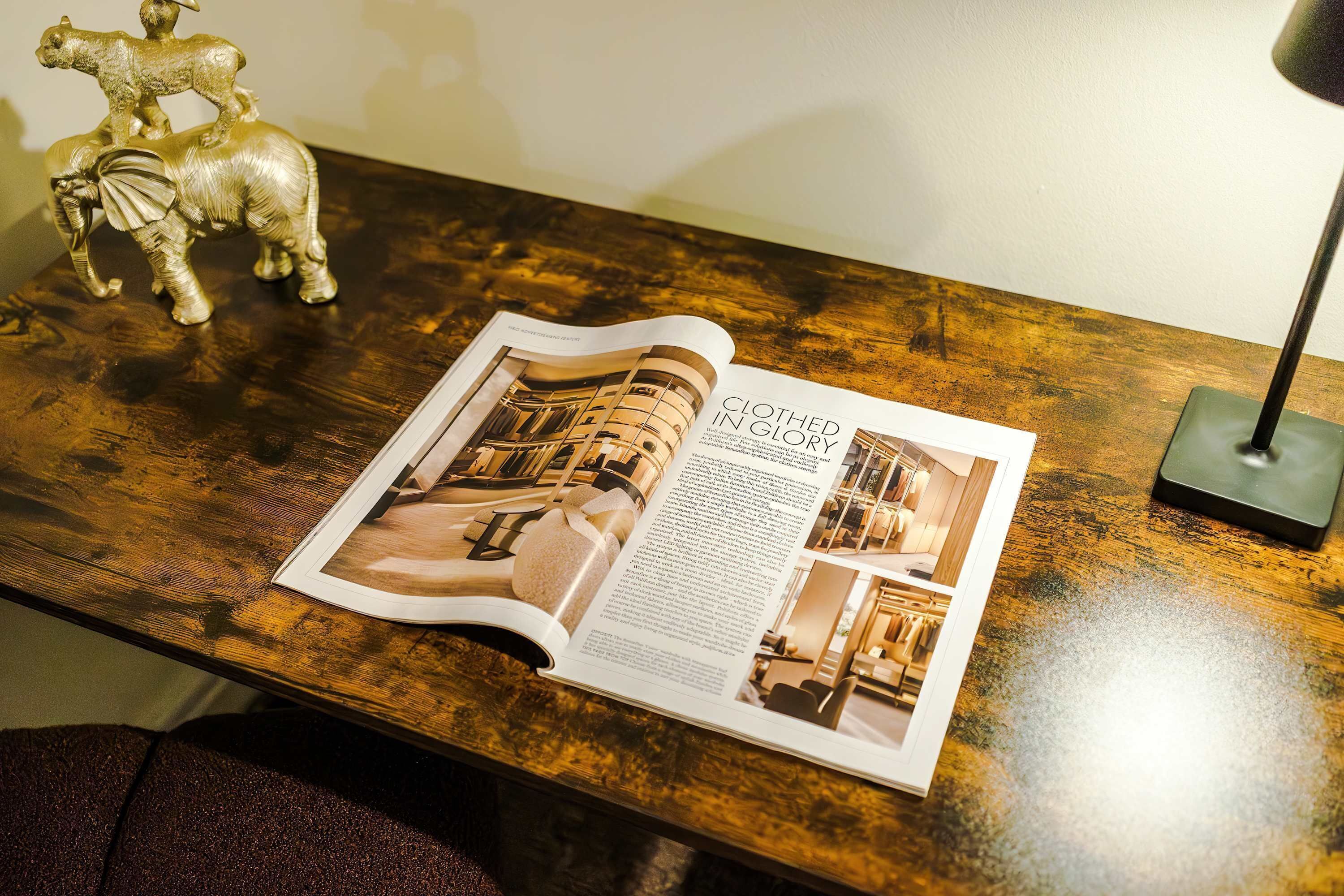 Revista aberta sobre uma mesa de madeira, com uma página intitulada 'Clothed in Glory' e imagens do interior de um quarto de hotel.