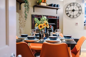 A dining area with a table set for four, a large wall clock, and a fireplace. - Charming City Centre 3 Bed Flat High St Location (Chester)