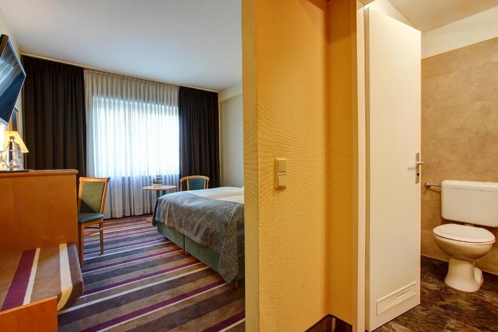 Une chambre d’hôtel comprenant un lit, un bureau avec une chaise, une télévision et une salle de bain avec des toilettes.