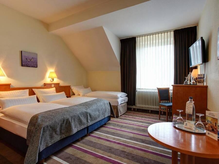 A hotel room with two beds, a desk, a chair, a television, and a window with curtains.