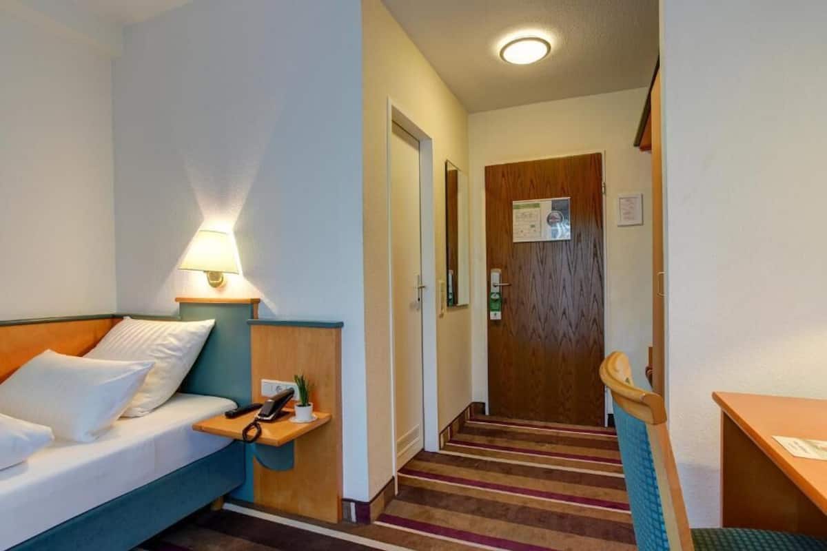 A hotel room with a bed, bedside table, lamp, and a wooden door.