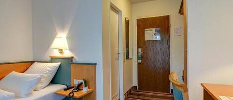 Une chambre d’hôtel avec un lit, une table de chevet, une lampe et une porte en bois.