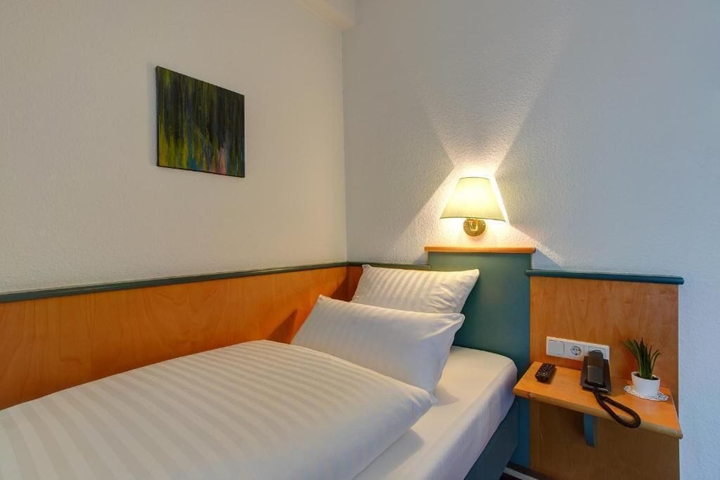 A hotel room with a bed, a bedside lamp, a phone, and a small plant on a nightstand.