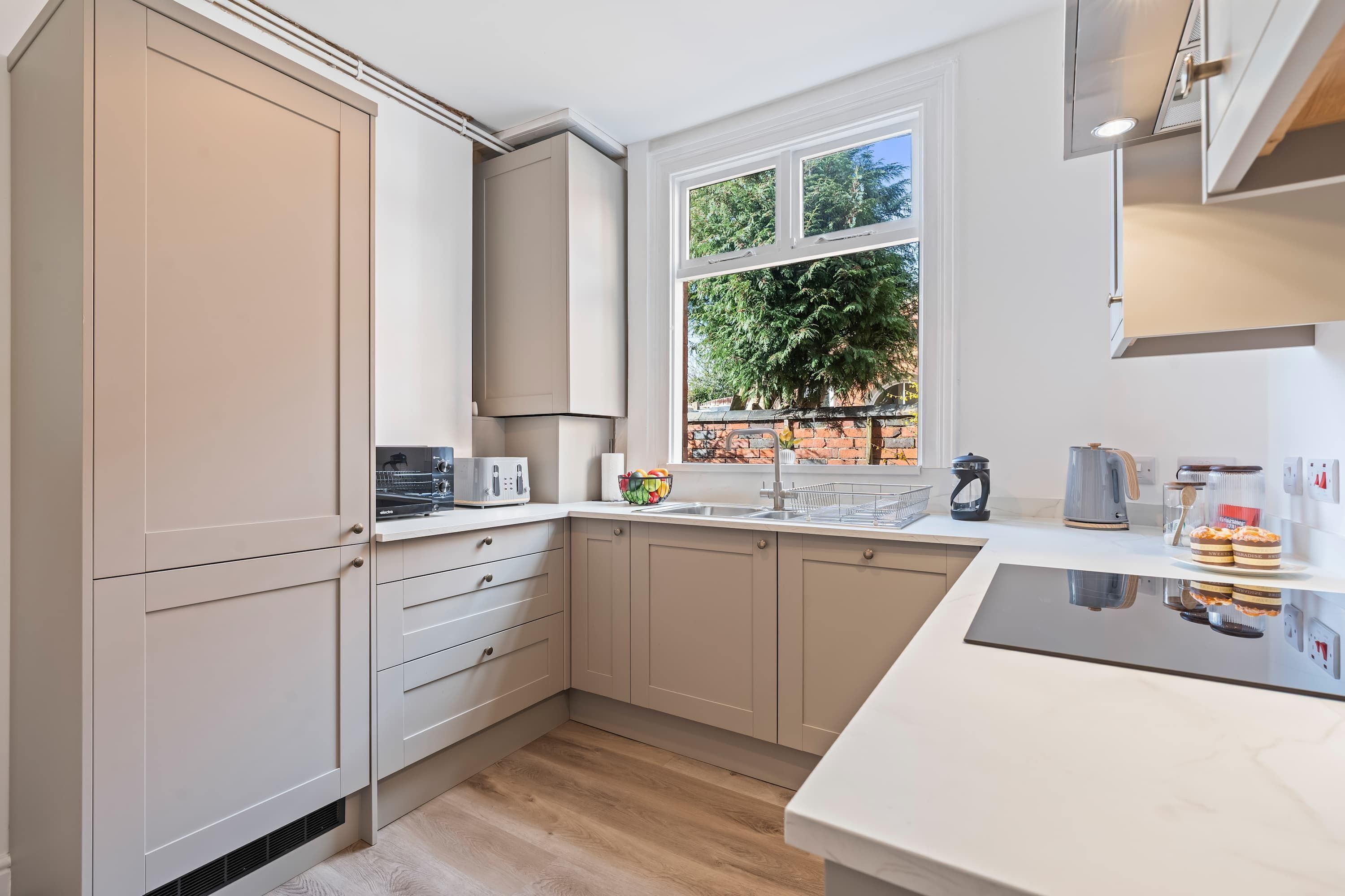 A modern kitchen with white cabinets, a built-in oven, and a window with a view of trees.
