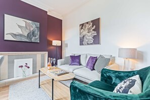 A modern living room with a sofa, a green armchair, a coffee table, and two wall-mounted lamps. - Beautiful Large Home in Cradley Heath Sleeps 8 (Cradley Heath)