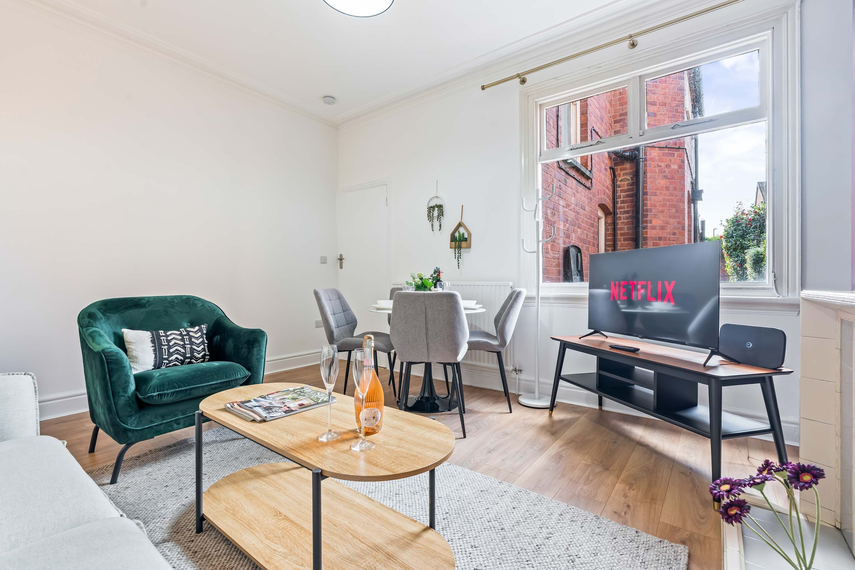 A modern living room with a green armchair, a wooden coffee table, a dining area with a table and chairs, and a TV displaying 'NETFLIX'.
