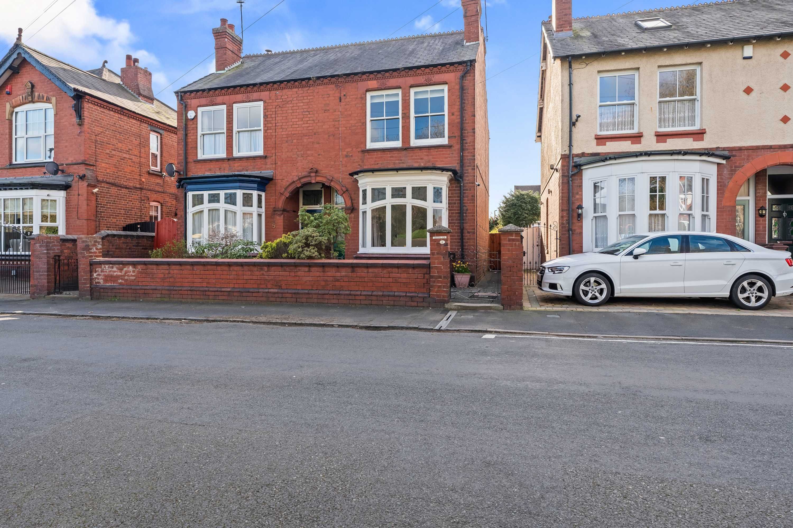A residential street with houses, a white car parked on the right, and a clear sky.
