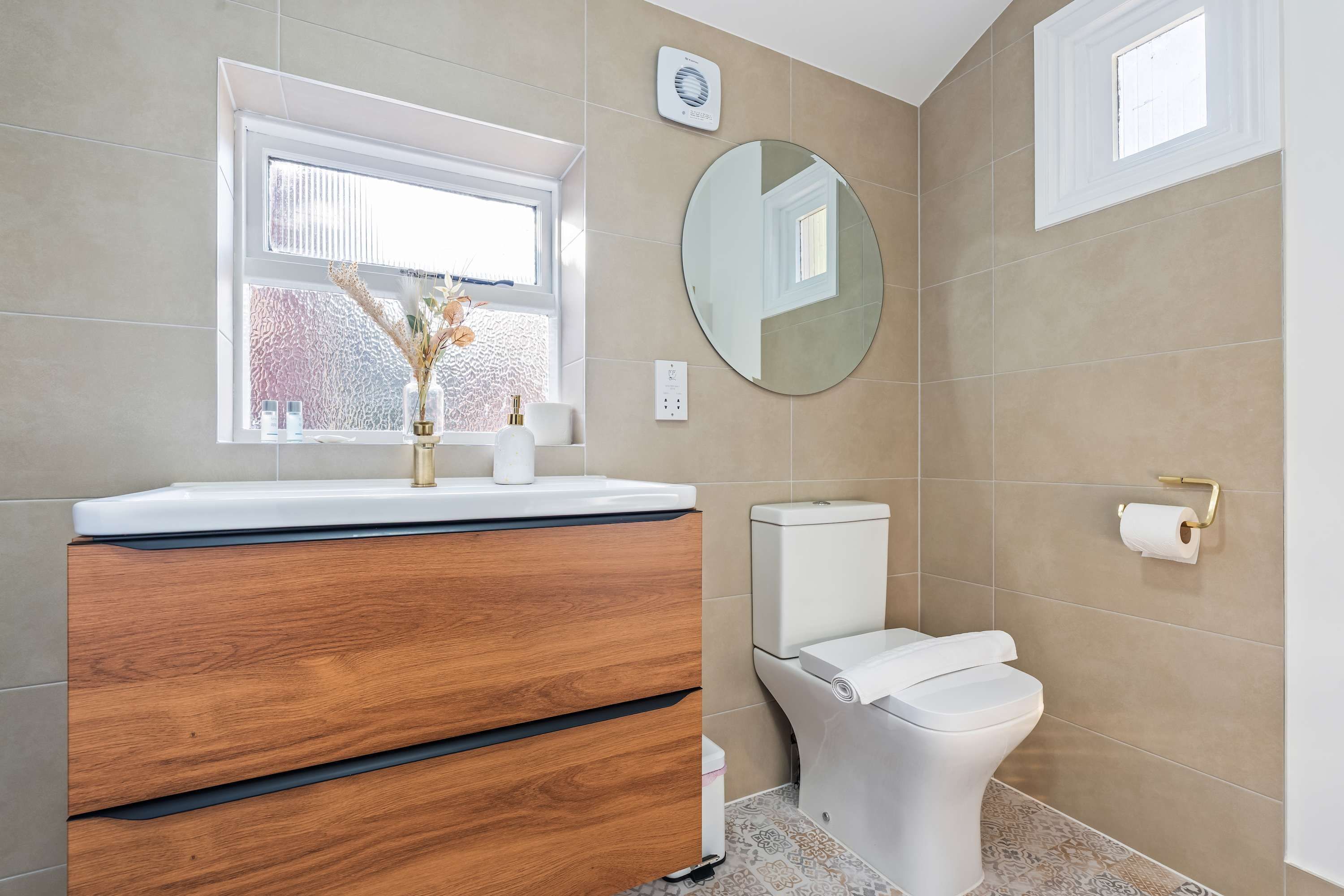 Een badkamer met een houten wastafel, toilet, ronde spiegel en raam.