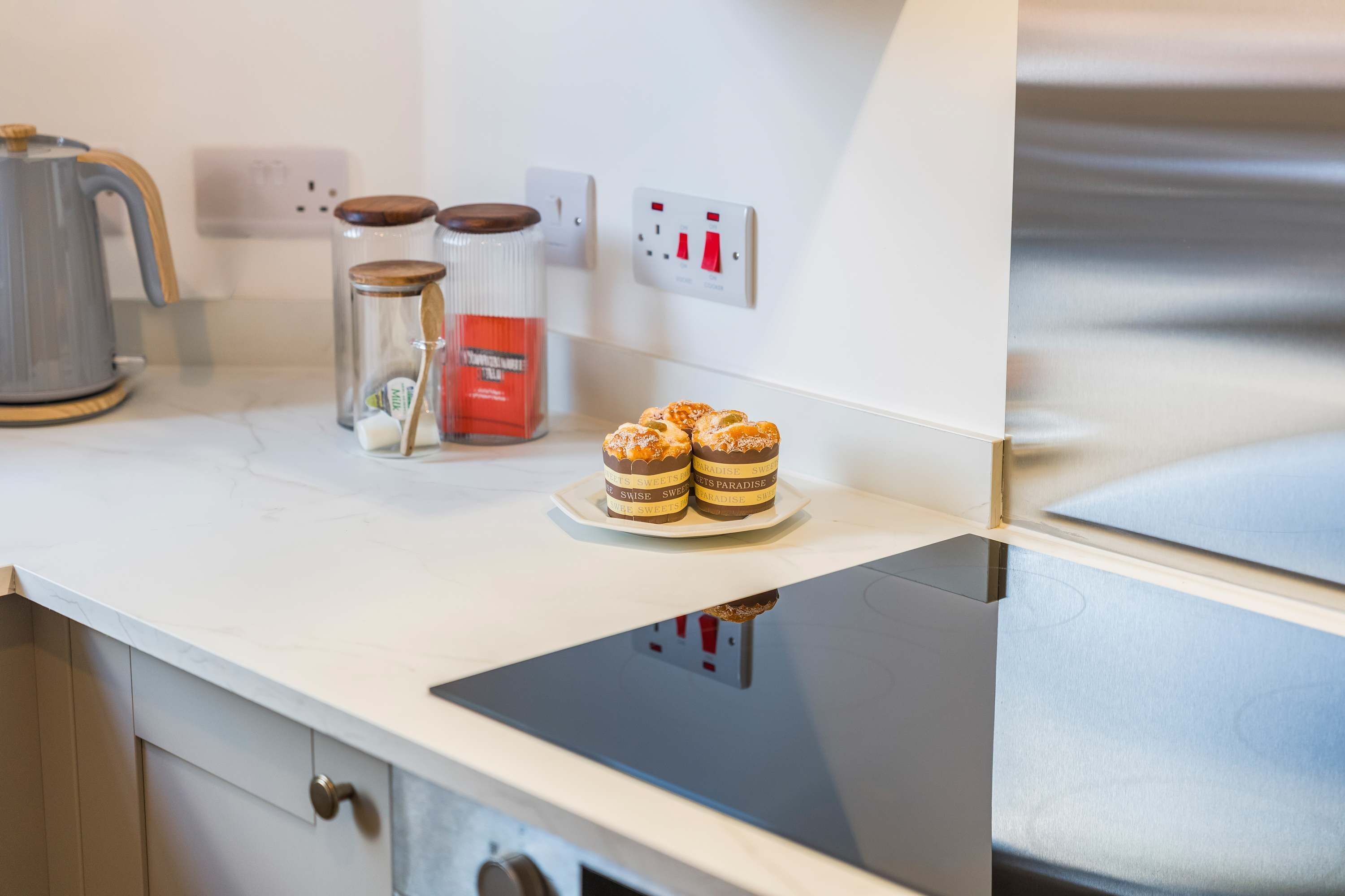 A kitchen counter with a coffee maker, two jars, and a plate with two pastries.