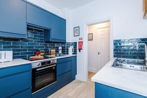 A modern kitchen with blue cabinets, a white countertop, a stainless steel sink, and a tiled backsplash. - Spacious 4 Bed Home in Crewe Perfect for Groups (Crewe)