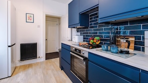 Una cocina moderna con armarios azules, horno integrado y encimera con frutero y cafetera.