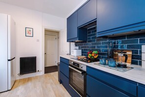 A modern kitchen with blue cabinets, a built-in oven, and a countertop with a fruit bowl and coffee maker. - Spacious 4 Bed Home in Crewe Perfect for Groups (Crewe)