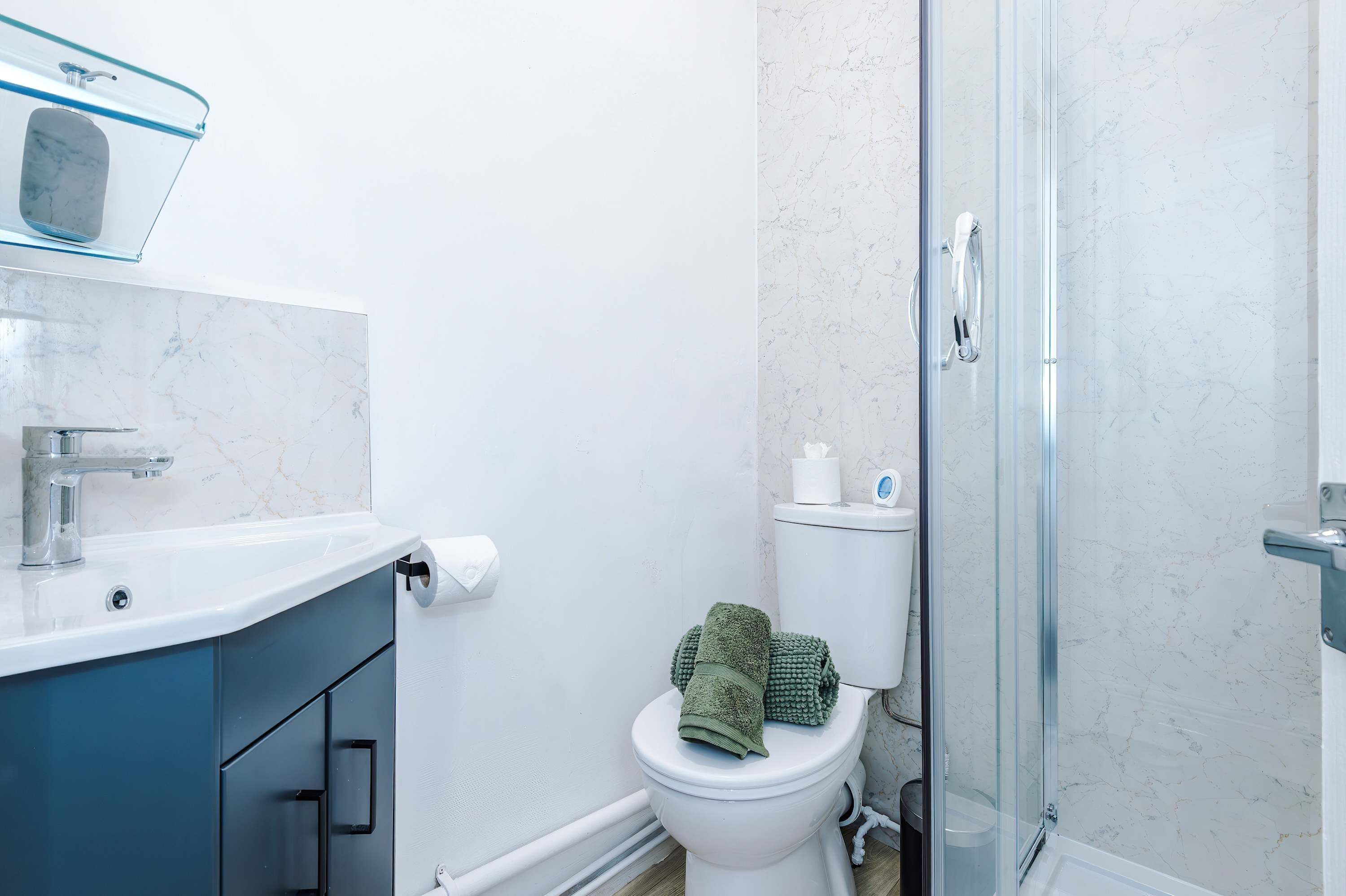 Ein Badezimmer mit Toilette, einer Duschkabine aus Glas und einem blauen Schrank mit Seifenschale.
