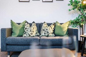 Un canapé gris agrémenté de coussins à motifs, une petite table et une plante en pot dans un salon moderne.