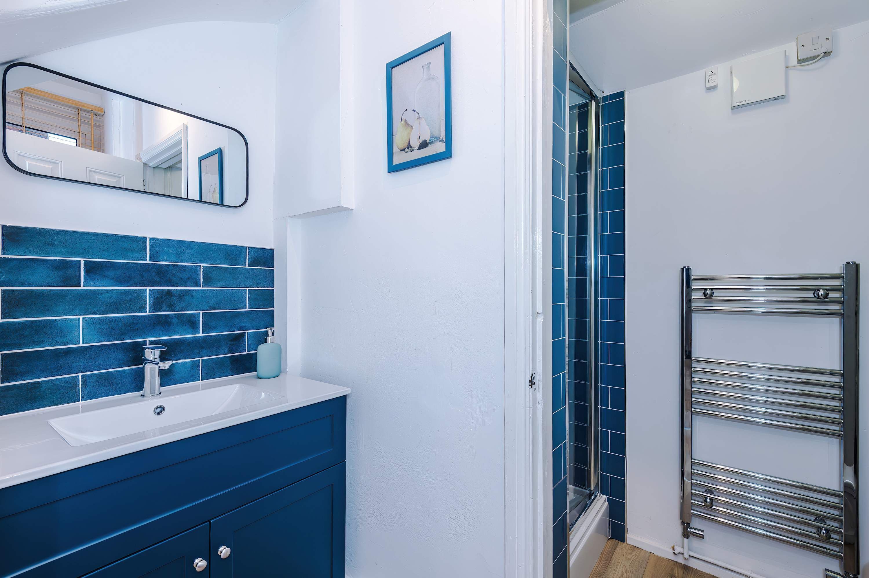 Een badkamer met een wit wastafelmeubel, blauwe tegels, een spiegel en een handdoekhouder.